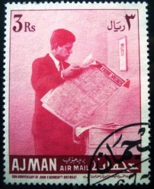 Selo postal de Ajman de 1967 Kennedy reading newspaper